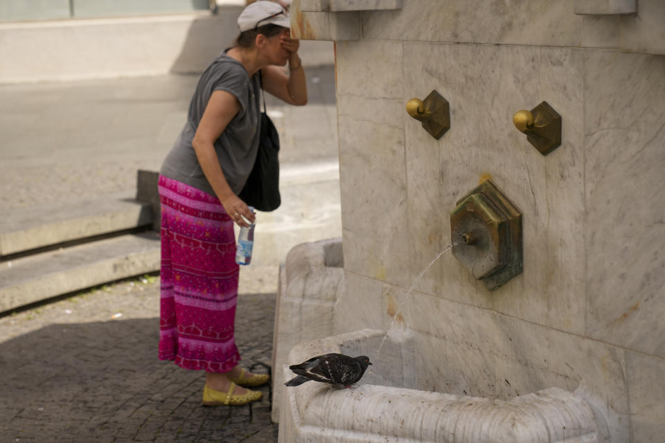 A woman cools herself as a pigeon drinks water from a public fountain in Belgrade, Serbia, Friday, June 21, 2024. A major hourslong power outage hit much of the Balkans on Friday as the southern European region sweltered in an early heat wave that sent temperatures soaring to more than 40 C (104 F). (AP Photo/Darko Bandic)