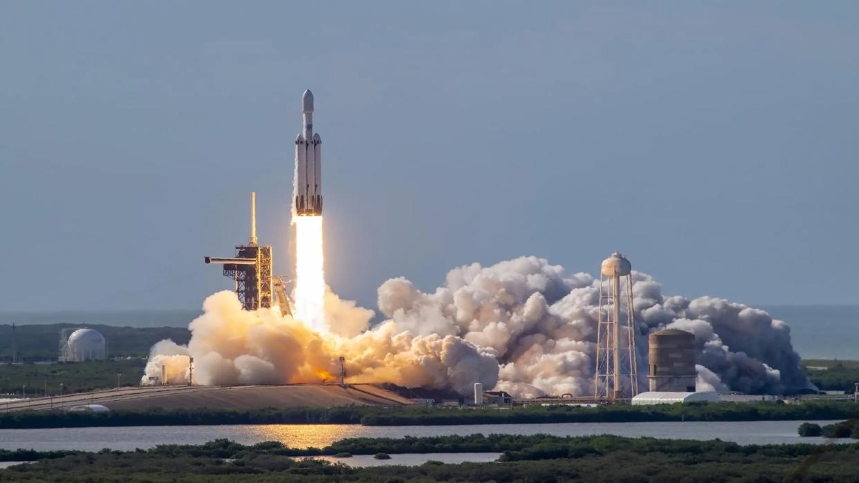  A big white rocket launches into a blue sky, with the ocean in the background. 