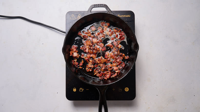 bacon bits cooking in cast iron skillet