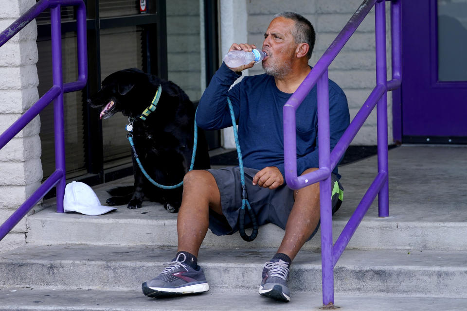 Martin Brown and his dog Sammy try to keep cool outside the Circle In The City homeless clinic, Monday, July 10, 2023, in Phoenix. (AP Photo/Matt York)