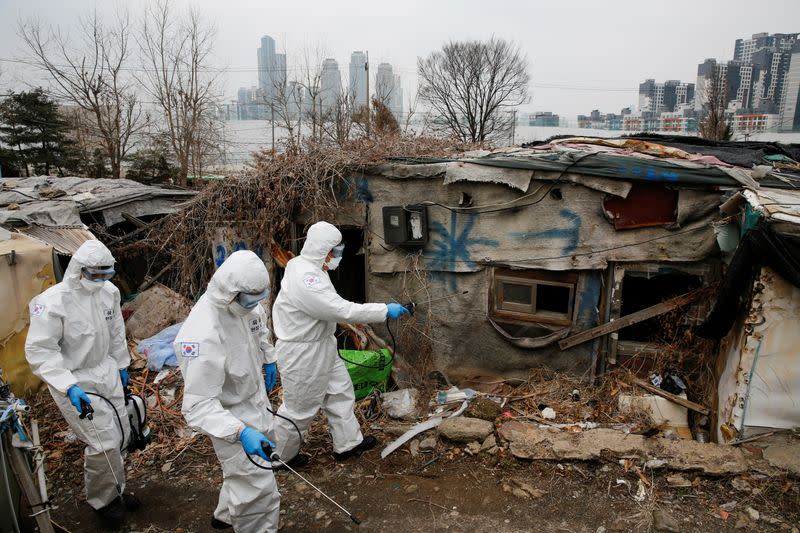 South Korean soldiers in protective gears sanitize shacks as a luxury high-rise apartment complex is seen in the background at Guryong village in Seoul