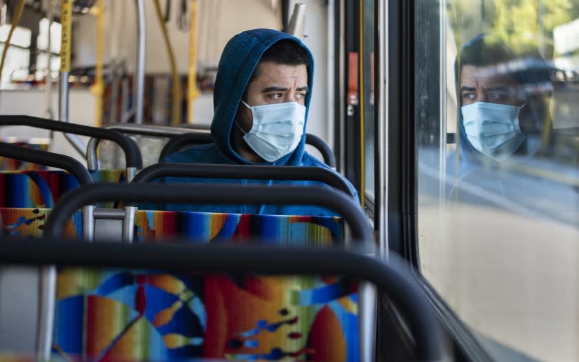 WOODLAND HILLS, CALIF. -- FRIDAY, MARCH 27, 2020: Danny Armada sits with his own reflection in the window of an early morning Orange Line bus in Woodland Hills, Calif., on March 27, 2020. The coronavirus pandemic is causing ridership on LA Metro trains and busses to plummet. (Brian van der Brug / Los Angeles Times)