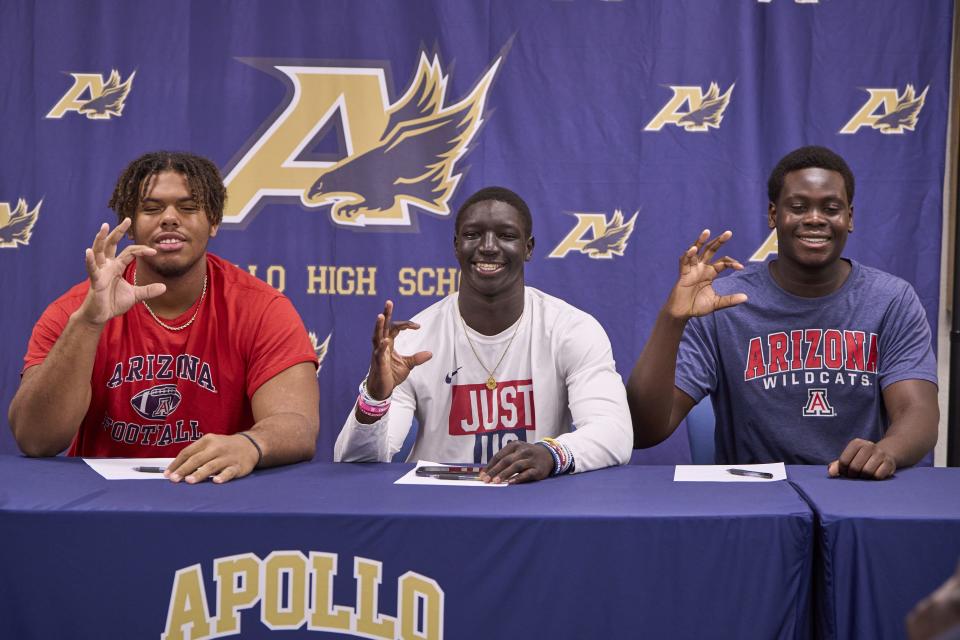 (L-R) Apollo Hawks Offensive lineman Michael Watkins, running back Adam Mohammed and offensive lineman Matthew Lado hold up the Wildcat hand symbol after they sign their commitment papers to the University of Arizona at Apollo High School in Glendale on Dec. 20, 2023.