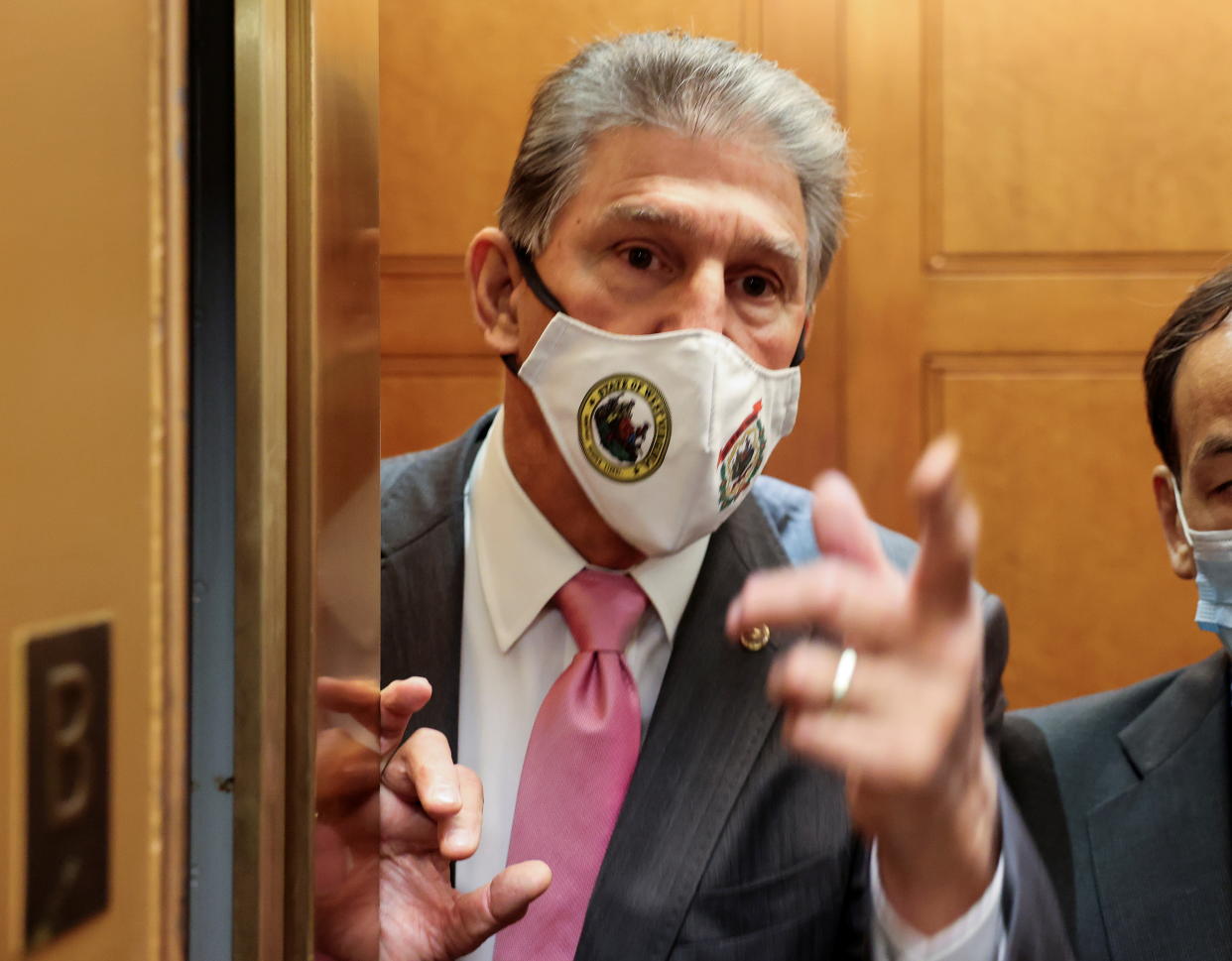 Joe Manchin, wearing a face mask, gestures with his hand from an elevator.