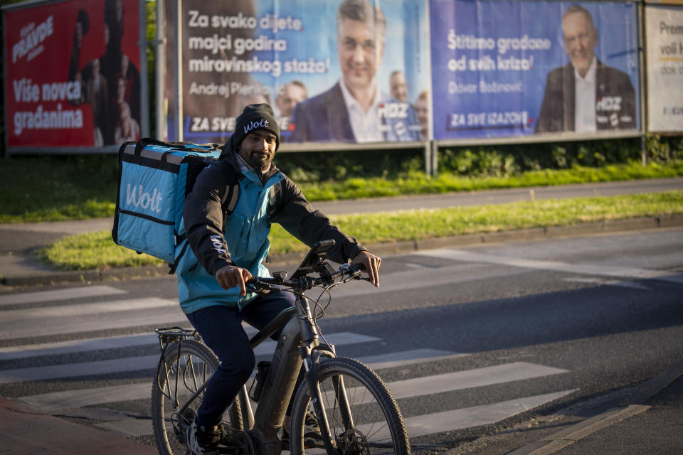 A delivery man rides a bicycle in front of election posters in Zagreb, Croatia, Sunday, April 14, 2024. Croatia this week holds an early parliamentary election following a campaign that was marked by heated exchanges between the country's two top officials, creating a political crisis in the Balkan country, a European Union and NATO member state. (AP Photo/Darko Bandic)