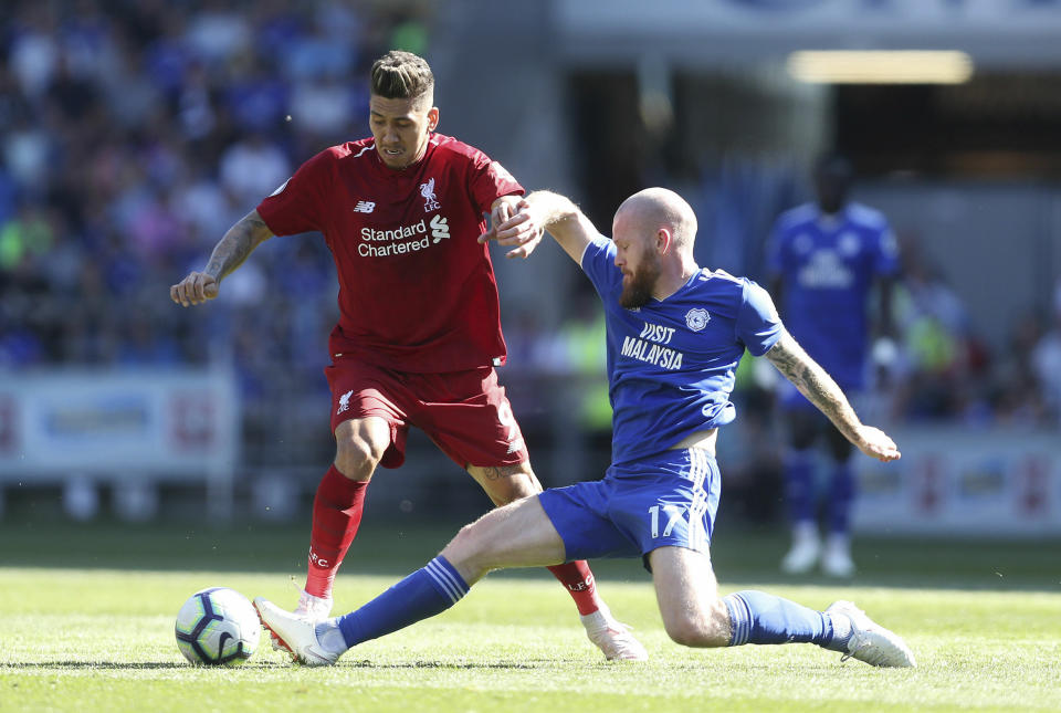 Liverpool's Roberto Firmino and Cardiff City's Aron Gunnarsson, right, battle for the ball during the English Premier League soccer match at The Cardiff City Stadium, Cardiff, Wales, Sunday April 21, 2019. (David Davies/PA via AP)