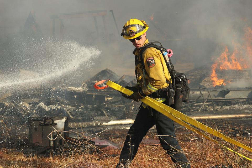 Firefighters battling the Peter Fire near Anderson spray water on structures that burned up on the 19000 block of Spring Gulch Road on Thursday, July 14, 2022.