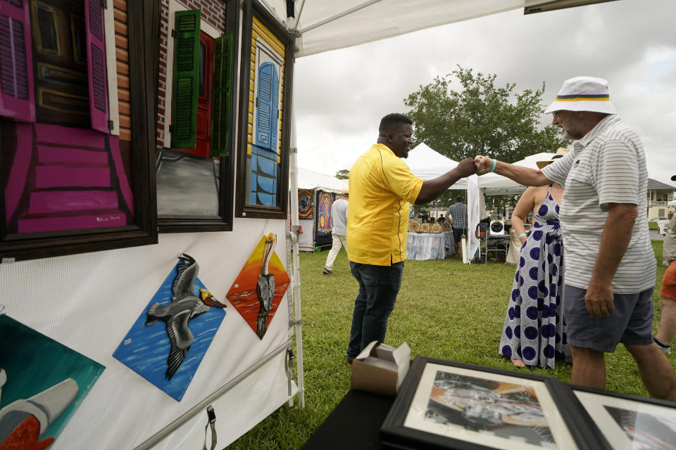 Local artist Patrick Henry greets a visitor near some of his paintings of pelicans for sale at the Bayou Boogaloo festival in New Orleans, Saturday, May 21, 2022. The large coastal birds were among the first species declared endangered in the U.S. in 1970. But a long-running effort to bring them back led to one of the country’s most inspiring comeback stories. (AP Photo/Gerald Herbert)