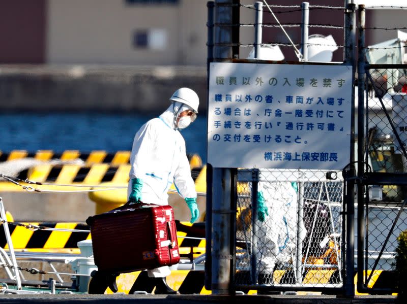 An officer in protective gears carry a luggage cases after people who were transferred from cruise ship Diamond Princess arrived at a maritime police's base in Yokohama