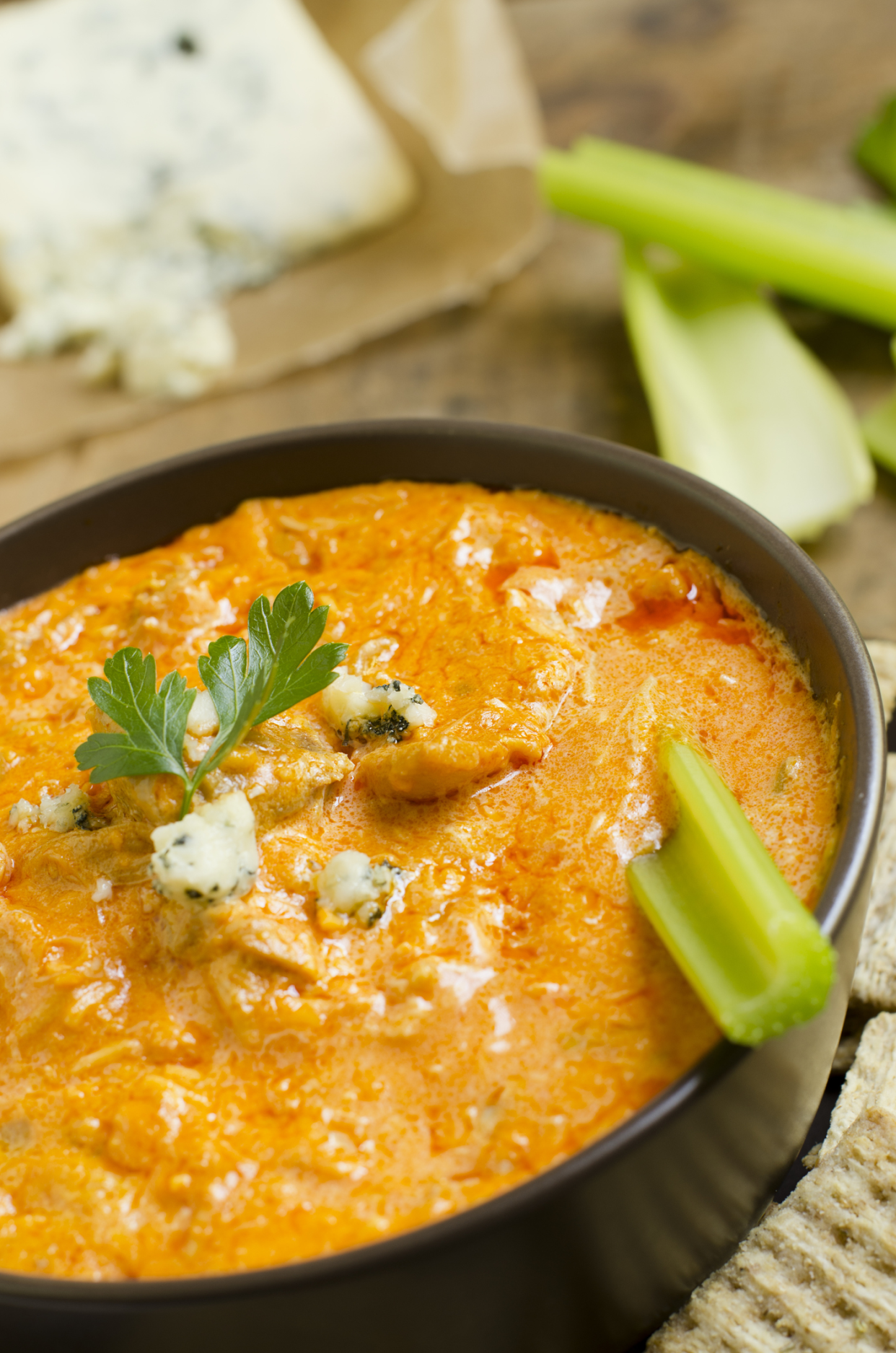 Spicy Greek feta dip, Tyrokafteri, with a stick of celery in a black bowl, selective focus, surrounded by Triscuit crackers, celery, and feta cheese, blurred in the background