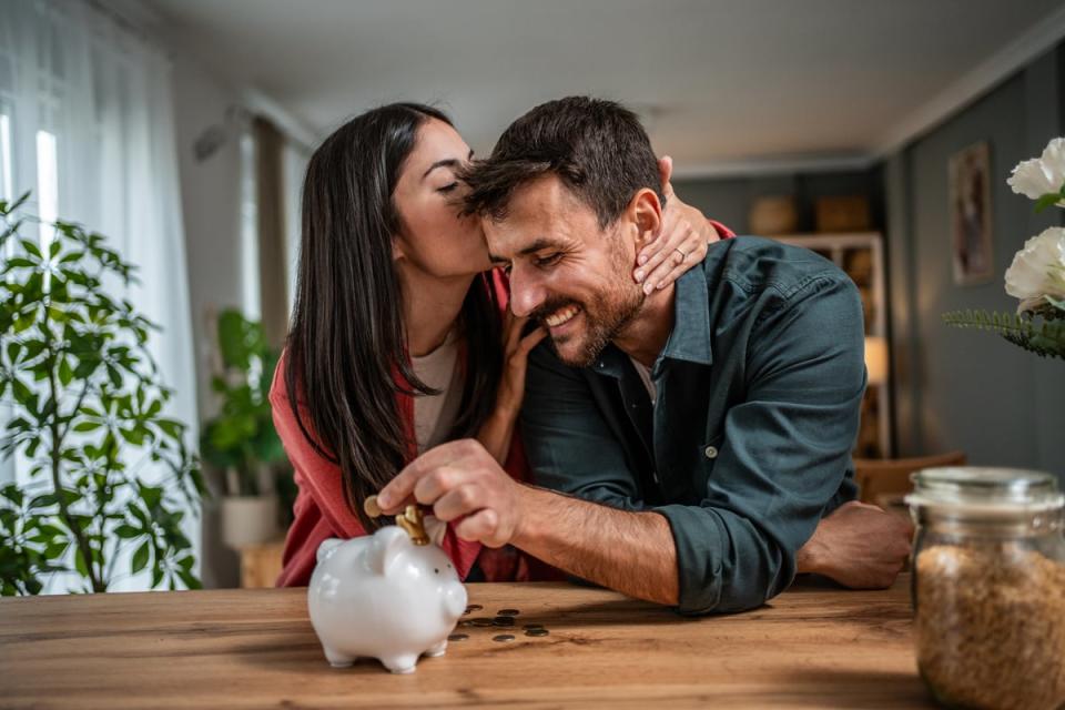 Two happy people with one putting money into a piggybank.