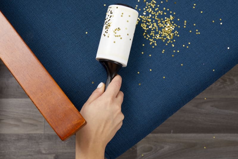 Close up of a hand holding a lint roller and using it to clean up glitter on a chair cushion.