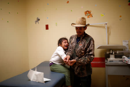 Honduran migrant Alvin Reyes, 39, holds the hand of his daughter Maria, 6, as she receives medical treatment after crushing her finger in a door, at a hospital in Puebla, Mexico, November 12, 2018. REUTERS/Carlos Garcia Rawlins