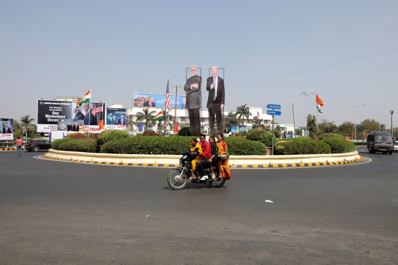 A family ride a scooter in front of cutouts of India's Prime Minister Narendra Modi and U.S. President Donald Trump along a road, ahead of Trump's visit, in Ahmedabad