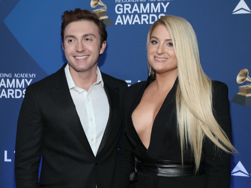 daryl sabara and meghan trainor at the 2019 delta air lines grammys party. they're wearing both black suits, sabara's with a white shirt, and trainor's open, showing her cleavage