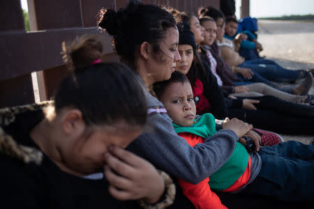 Immigrants sit along the border wall as they await apprehension after illegally crossing into the U.S. from Mexico on August 29, 2018. REUTERS/Adrees Latif