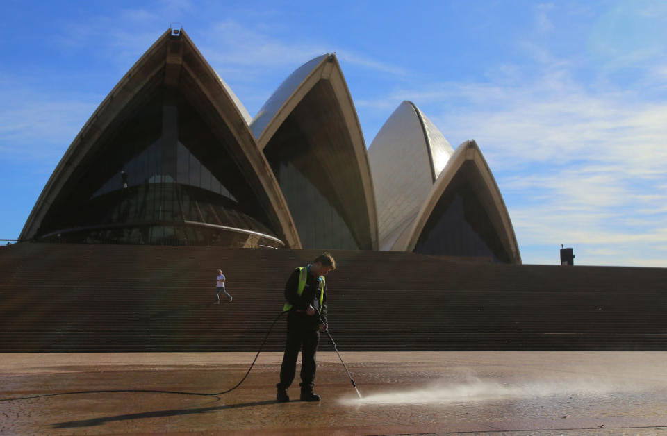 A worker uses a water-blaster to clean the ground in front of the Sydney Opera House.