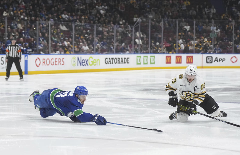 Vancouver Canucks' Teddy Blueger, front left, dives to swat the puck away from Boston Bruins' Brad Marchand, right, during the second period of an NHL hockey game in Vancouver, British Columbia, Saturday, Feb. 24, 2024. (Darryl Dyck/The Canadian Press via AP)