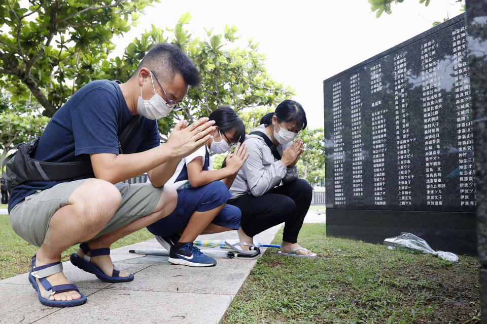Members of a bereaved family pray in front of a "Cornerstone of Peace" monument wall on which the names of all those who lost their lives, both civilians and military of all nationalities in the Battle of Okinawa are engraved, at the Peace Memorial Park in Itoman, Okinawa, Japan, Tuesday, June 23, 2020. Okinawan people find it unacceptable that their land is still occupied by a heavy U.S. military presence even 75 years after World War II. They have asked the central government to do more to reduce their burden, and Japanese Prime Minister Shinzo Abe's government repeatedly say it is mindful of their feelings, but the changes are slow to come. (Kyodo News via AP)