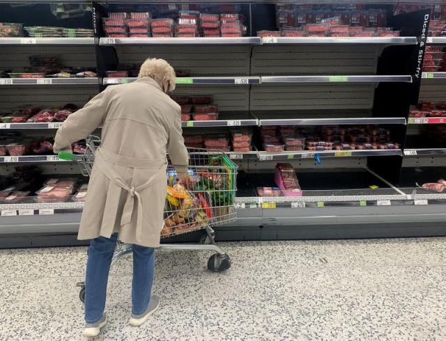 A shopper stands in front of empty shelves in the meat aisle of a supermarket in Liverpool