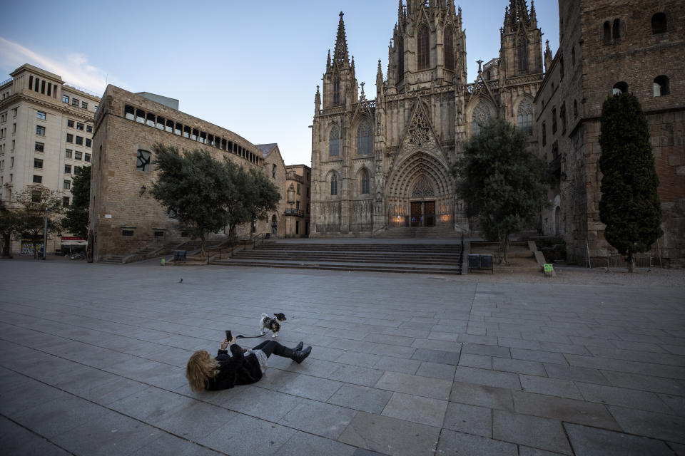 A woman takes a photo of her dog in front of the Barcelona's cathedral, Spain, Sunday, March 15, 2020. Spain's government announced Saturday that it is placing tight restrictions on movements and closing restaurants and other establishments in the nation of 46 million people as part of a two-week state of emergency to fight the sharp rise in coronavirus infections. For most people, the new coronavirus causes only mild or moderate symptoms. For some, it can cause more severe illness, especially in older adults and people with existing health problems. (AP Photo/Emilio Morenatti)