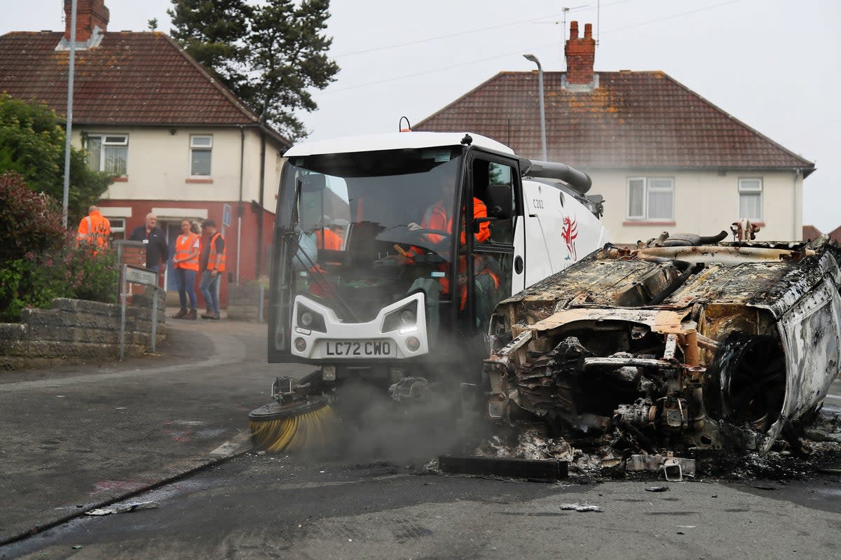 Council workers clear debris from the area immediately around a car that was set alight in El (PA)