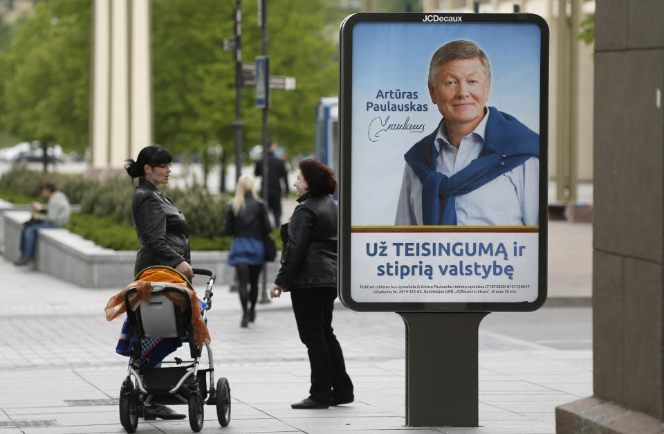 Local residents stand near an election poster showing Lithuanian Labour Party leader Arturas Paulauskas, a presidential candidate, in Vilnius, Lithuania, Friday, May 9, 2014. The poster reads " For justice and a strong state." Lithuanians will ballot Sunday, May 11, in a first round of presidential elections. (AP Photo / Mindaugas Kulbis)