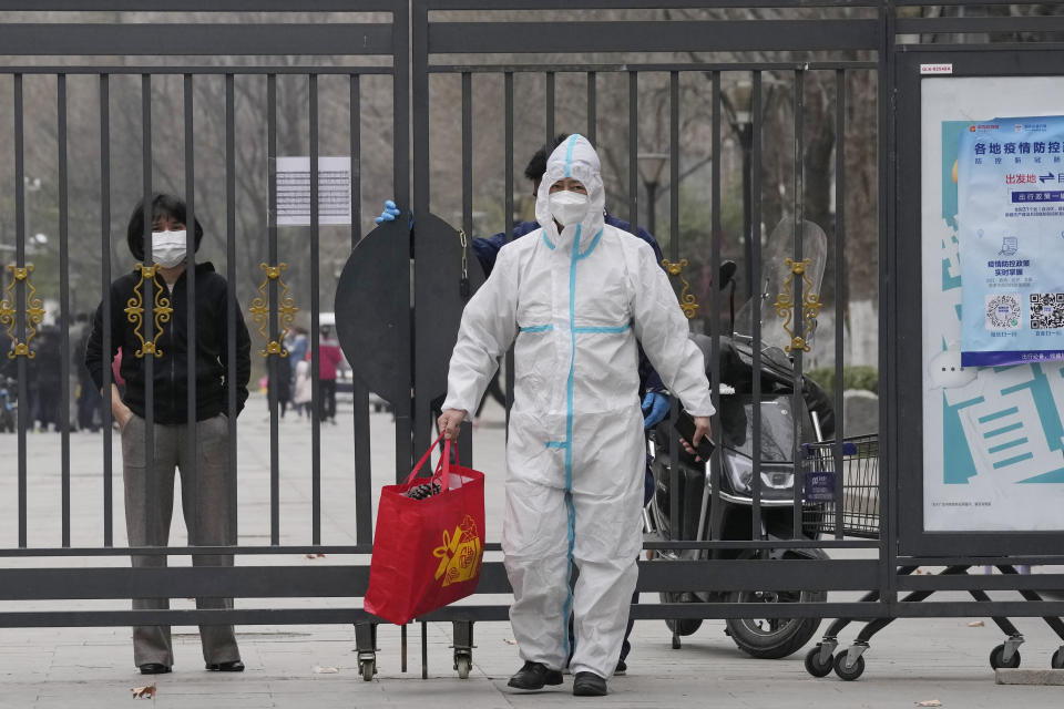 A worker in protective gear helps pass on a bag from a resident inside a locked down community on Sunday, March 13, 2022, in Beijing. The number of new coronavirus cases in an outbreak in China's northeast tripled Sunday and authorities tightened control on access to Shanghai in the east, suspending bus service to the city of 24 million and requiring a virus test for anyone who wants to enter. (AP Photo/Ng Han Guan)