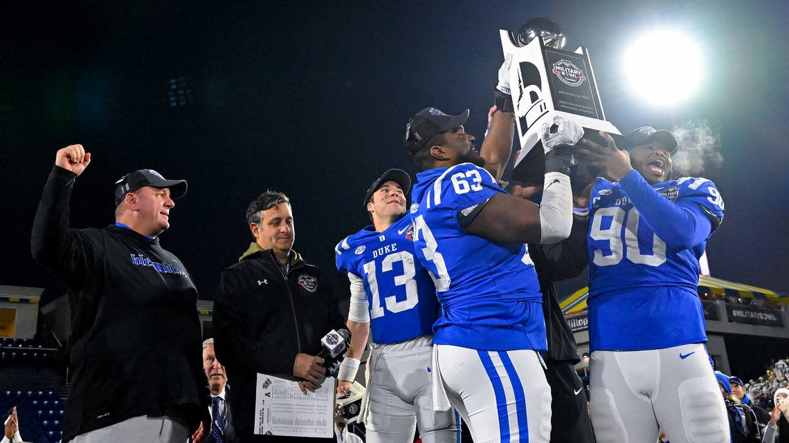 Duke offensive lineman Jacob Monk (63), defensive tackle DeWayne Carter (90) and quarterback Riley Leonard (13) hold the Military Bowl trophy as head coach Mike Elko, left, cheers after the Military Bowl NCAA college football game against UCF, Wednesday, Dec. 28, 2022, in Annapolis, Md. (AP Photo/Terrance Williams)