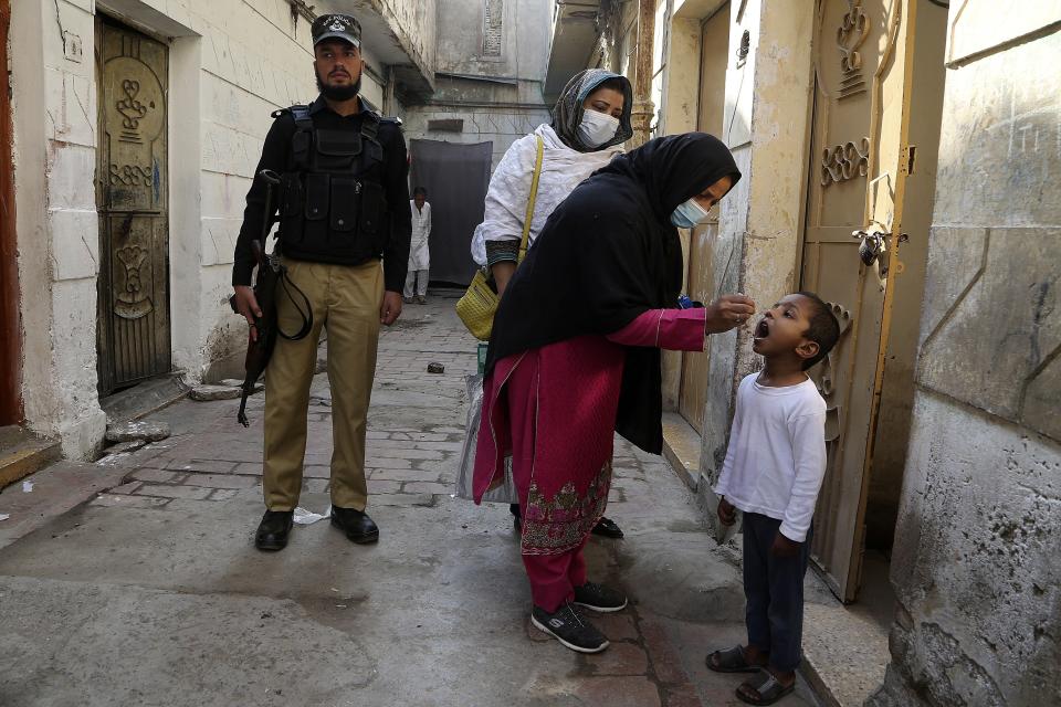 A police officer stands guard while a health worker gives a polio vaccine to a child in Peshawar, Pakistan, Monday, Oct. 24, 2022. (AP Photo/Muhammad Sajjad)