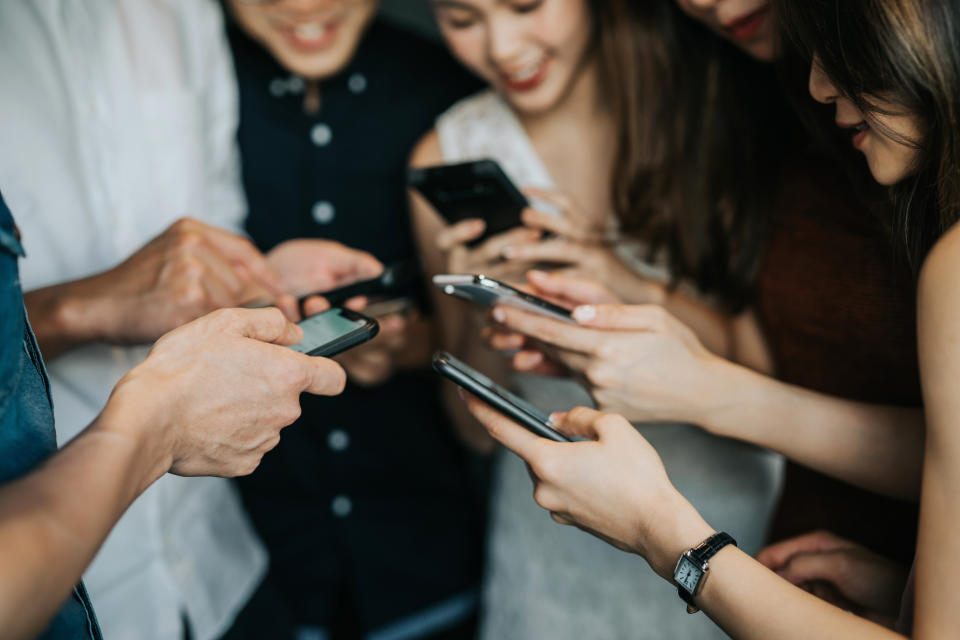 Circle of young Asian man and woman using smartphone during party