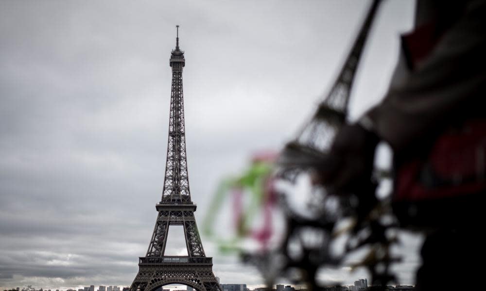 A man selling souvenirs stands in front of the Eiffel Tower in Paris.