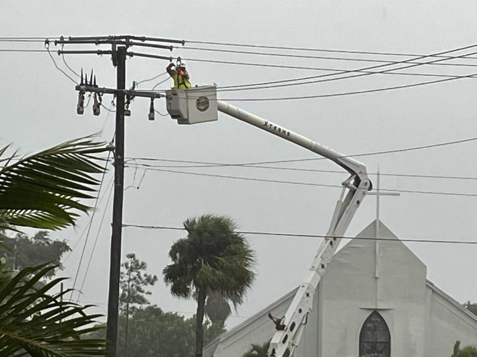 A line man working in a rain high in a bucket, up next to some live lines in Satellite Beach, at the intersection of Cassia Boulevard and Temple Street, in front of the Oceanside Community Church.