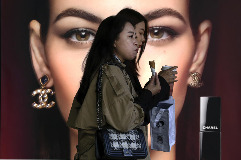 FILE - In this Oct. 19, 2020, file photo, women eating snack walk by a Chanel cosmetic shop at the capital city's popular shopping mall in Beijing. China’s economy grew 2.3% in 2020 as a recovery from the coronavirus pandemic accelerated while the United States, Europe and Japan struggled with disease flare-ups. (AP Photo/Andy Wong, File)