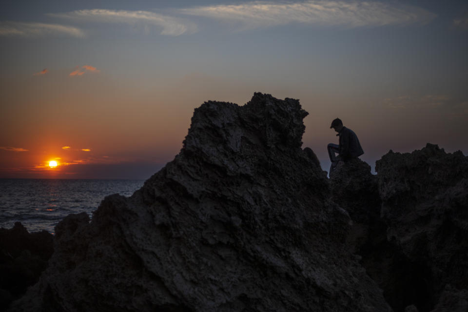 A boy sits on a rock as the sun sets over the Mediterranean Sea, in Gador nature reserve near Hadera, Israel, Sunday, Feb. 21, 2021. Israel has closed its Mediterranean beaches following an offshore oil spill that has devastated the country's coastline in what officials are calling one of the country's worst ecological disasters. The Environmental Protection, Health and Interior Ministries issued a joint statement Sunday warning the public not to visit beaches. (AP Photo/Ariel Schalit)