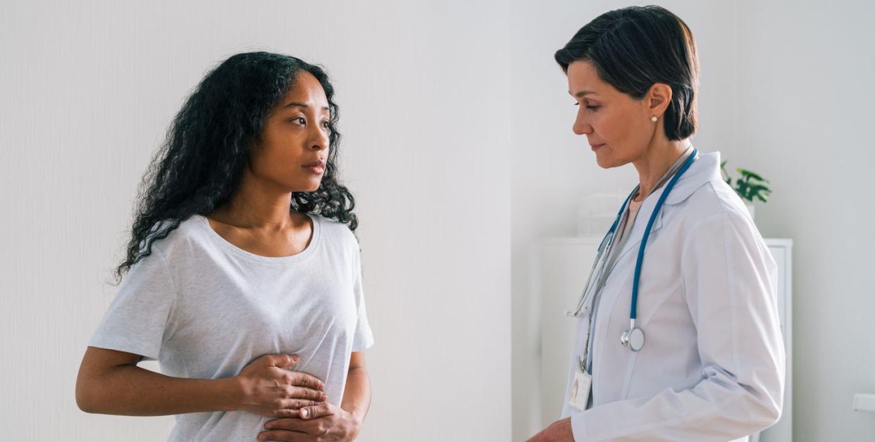 african american female patient touching belly and telling a mature worried doctor about stomachache at hospital appointment healthcare specialist showing concern about symptoms