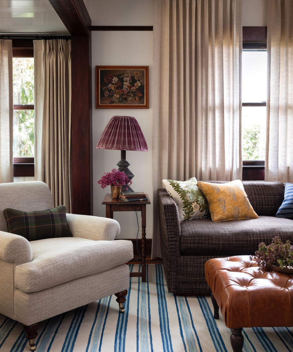 Cozy living room with sofa, armchair, leather ottoman, lampshades, beige curtains