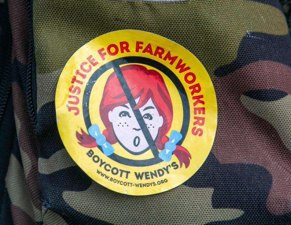 A woman wears a sticker on her backpack Friday urging people to boycott Wendy's at the start of a three-day Farmworker Freedom Festival.