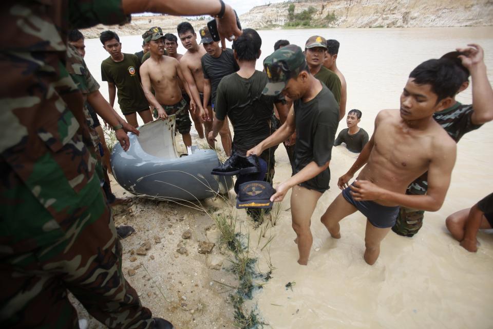 Rescue workers stand around a part of a Cambodian military helicopter, a cap and shoes which they salvaged after the helicopter crashed on the outskirts of Phnom Penh July 14, 2014. The military helicopter crashed on Monday, killing five and injured one, police told Reuters. A Cambodian air force official said authorities are still investigating the cause of the crash. (REUTERS/Samrang Pring)