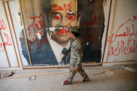 A fighters from the Iraqi Shi'ite Badr Organization looks at a poster depicting images of former Iraqi President Saddam Hussein on the outskirts of Falluja, Iraq, May 28, 2016. REUTERS/Thaier Al-Sudani