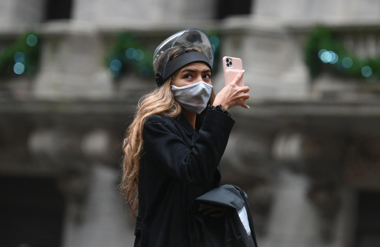 A woman wearing a face shield takes pictures with her mobile phone outside the New York Stock exchange (NYSE) at Wall Street on November 30, 2020 in New York City. - Credit ratings giant S&P Global reached an all-stock deal to buy IHS Markit for $44 billion, creating a massive enterprise to produce data and analytics used by Wall Street, the companies announced Monday. (Photo by Angela Weiss / AFP) (Photo by ANGELA WEISS/AFP via Getty Images)