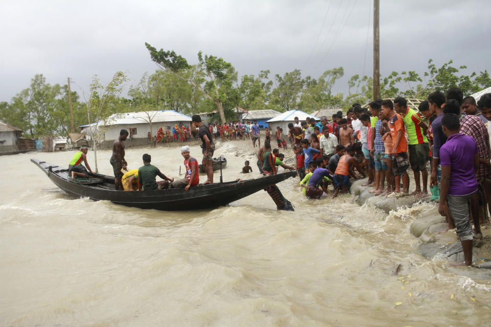 In this Wednesday, May 20, 2020 photo, a boat brings people to land, as locals check an embankment before Cyclone Amphan made landfall, in Shyamnagar, Shatkhira, Bangladesh. A powerful cyclone that slammed into coastal India and Bangladesh has left damage difficult to assess Thursday. (AP Photo/Abu Sufian Jewel)