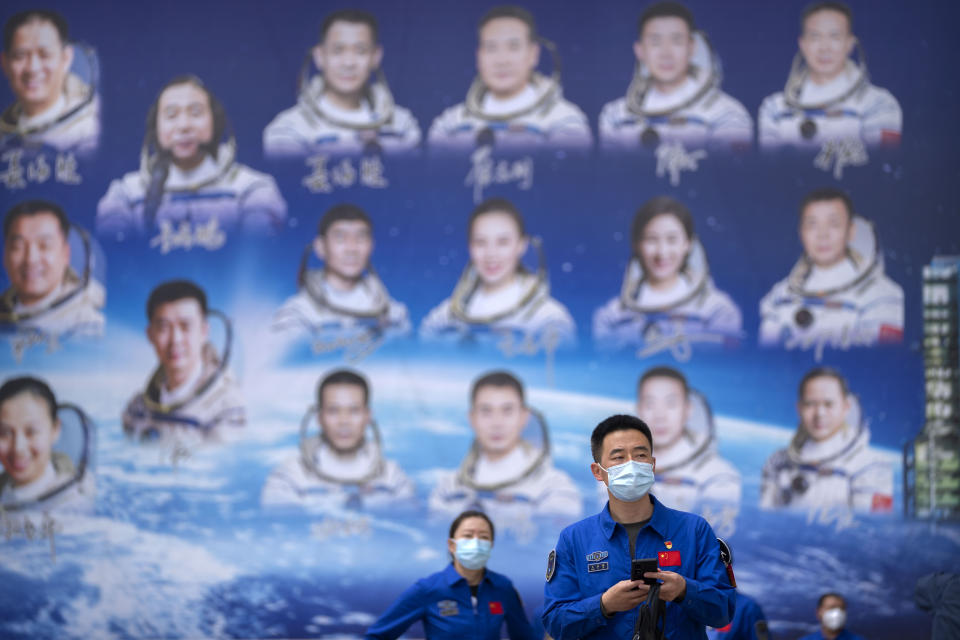 Staff members walk past a billboard depicting Chinese astronauts at the Jiuquan Satellite Launch Center in northwest China on Monday, May 29, 2023. China's space program plans to land astronauts on the moon before 2030, a top official with the country's space program said Monday. (AP Photo/Mark Schiefelbein)