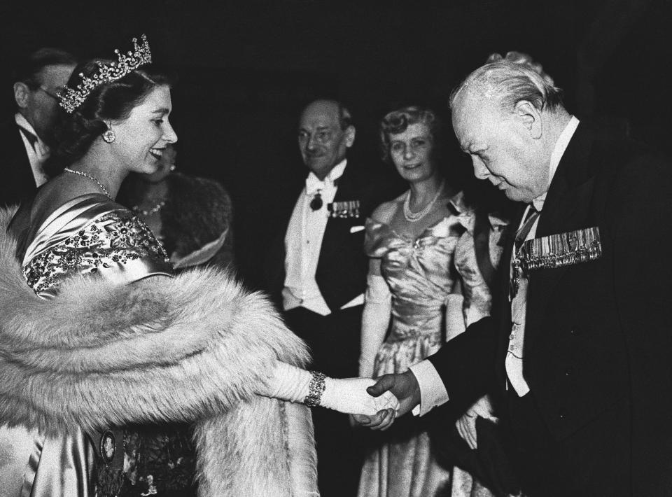 ARCHIVO – En esta fotografía de archivo del 22 de marzo de 1950 la princesa Isabel le da la mano al exprimer ministro británico Winston Churchill en una cena para celebrar el inicio del Fondo Nacional de Acción de Gracias en Londres. Al fondo está el primer ministro Clement Attlee y su esposa Violet. La la reina Isabel II, la monarca con el reinado más largo de Gran Bretaña, murió el jueves 8 de setiembre de 2022, a los 96 años de edad. (Foto AP, archivo)