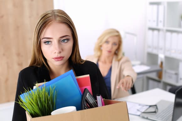 Worker carrying a box with office supplies with a sad facial expression.