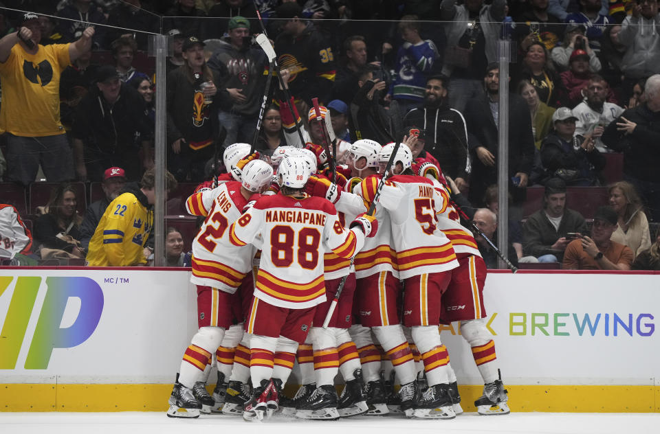 Calgary Flames' Tyler Toffoli is mobbed by teammates after his overtime goal against the Vancouver Canucks during an NHL hockey game Friday, March 31, 2023, in Vancouver, British Columbia. (Darryl Dyck/The Canadian Press via AP)