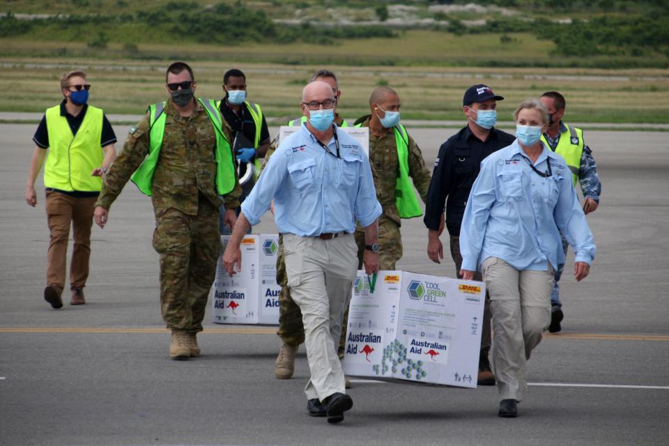 Australian officials carry boxes containing vaccines on PNG airstrip. 