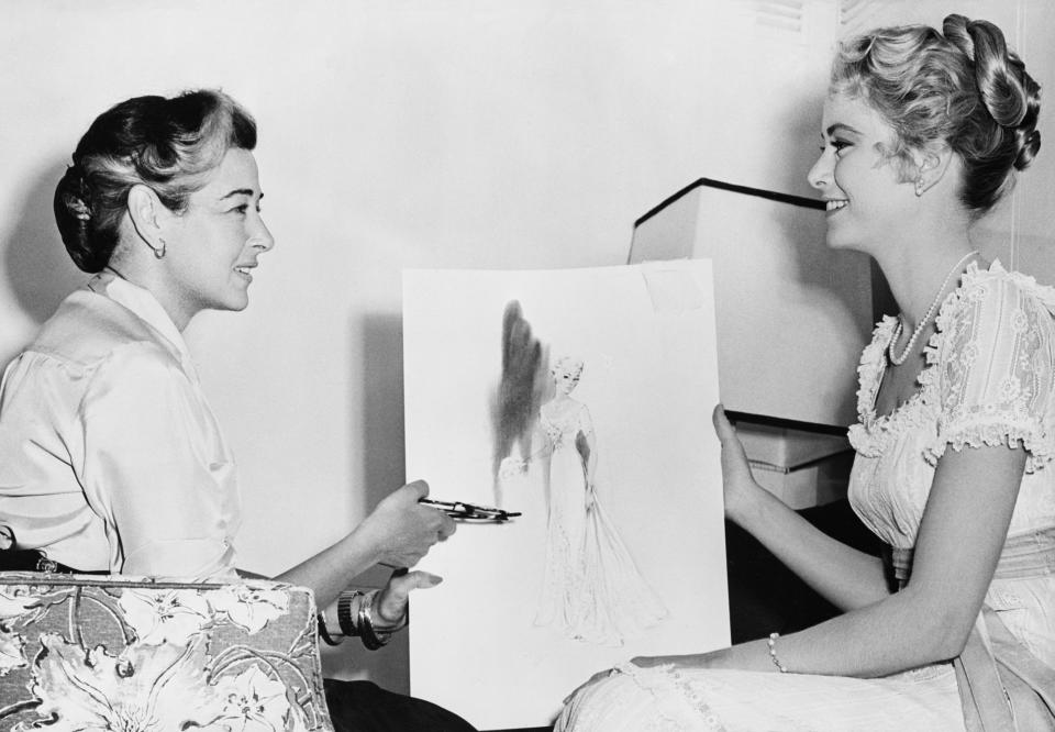 (Original Caption) 1/25/1956-Hollywood, CA: Although she has had offers from top designers all over the world, movie star Grace Kelly has selected Helen Rose, MGM designer to create her gown for her wedding to Prince Ranier III of Monaco sometime in April. Here is Miss Rose (l) and Miss Kelly going over a sketch for one of the star's gowns in her current film "High Society."