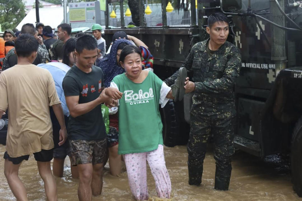 In this photo provided by the Philippine Coast Guard, rescuers assist a woman to safer grounds as floods rose due to Tropical Storm Nalgae at Parang, Maguindanao province, southern Philippines on Friday Oct. 28, 2022. (Philippine Coast Guard via AP)