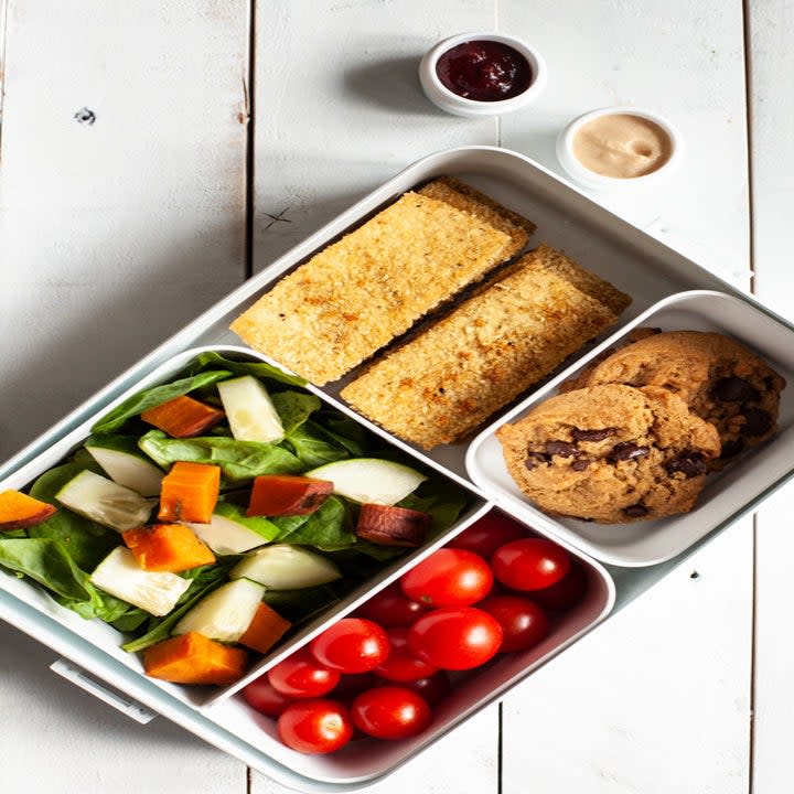 A bento box with cookies, salad, tomatoes, and tofu fingers